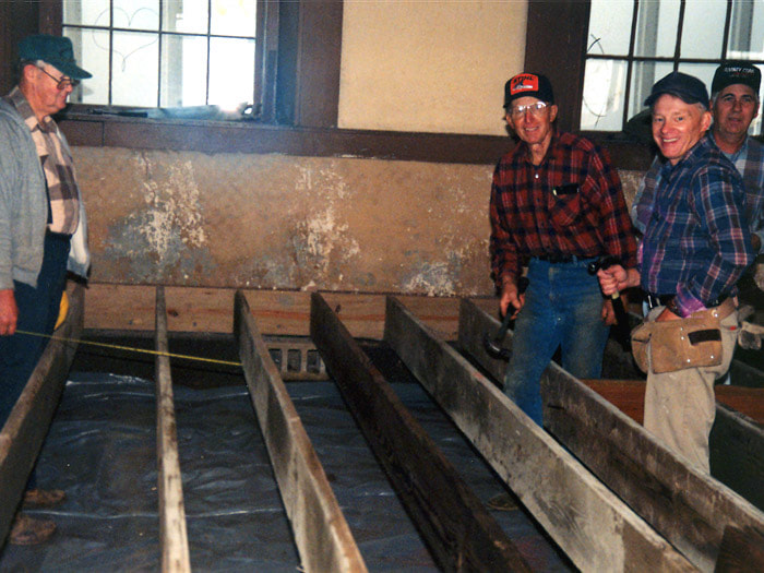 Volunteers stand in the floor joists as they work to remove and replace the flooring.